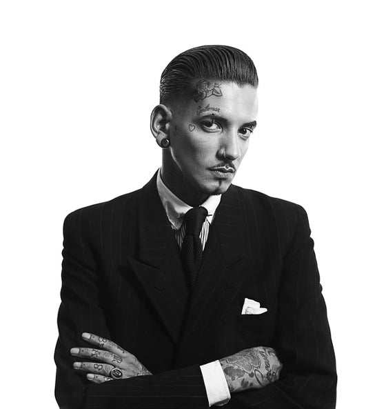 Schwarz-weiß-Porträt eines stilvollen Mannes mit Tattoos und Anzug, symbolisch für maskulinen Duft und gepflegte Haut durch Reuzel Aftershave Lotion Wood & Spice.