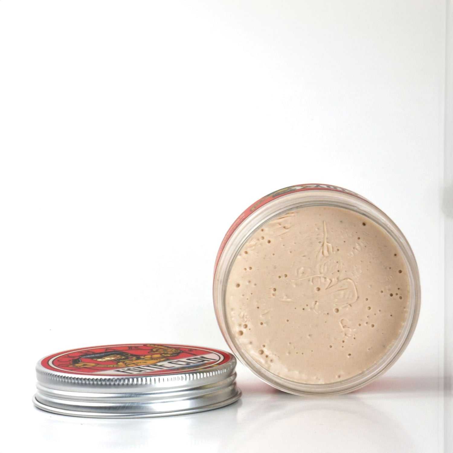Haarpomade Fätte Clay von Lockhart's mit starkem Halt und mattem Finish in offener Dose neben Deckel auf weißem Hintergrund