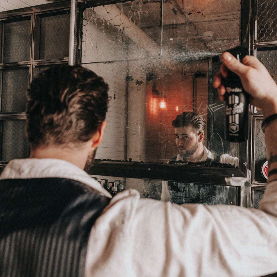 Mann sprüht Mootes Sea Salt Spray für natürliches, voluminöses Haar mit Strandfeeling vor Spiegel an.